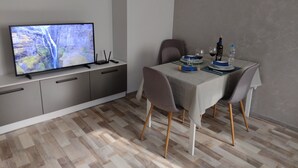 Un comedor moderno con un televisor de pantalla plana en un mueble, una mesa dispuesta con platos, vasos y una botella, y una silla.