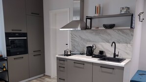 Una cocina moderna con gabinetes grises, horno empotrado, campana extractora de acero inoxidable, cafetera negra y un lavabo con grifo negro.