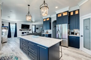 Una cocina moderna con gabinetes oscuros, una isla grande, electrodomésticos de acero inoxidable e iluminación colgante.