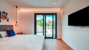 A modern bedroom with a large bed, a Mickey Mouse wall decoration, a TV mounted on the wall, and a sliding glass door to the outside.