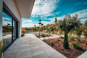 Een modern huis met een groot raam, een terras met zwembad en een tuin met diverse planten.