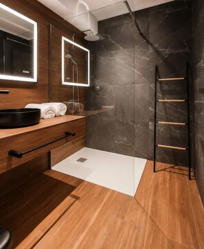Een moderne badkamer met een houten wastafelmeubel, een douchecabine met glazen wanden en een betegelde muur van marmer.