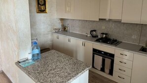 Une cuisine avec des meubles de couleur claire, un plan de travail en granit, une cuisinière, un évier et un petit objet décoratif accroché au mur.
