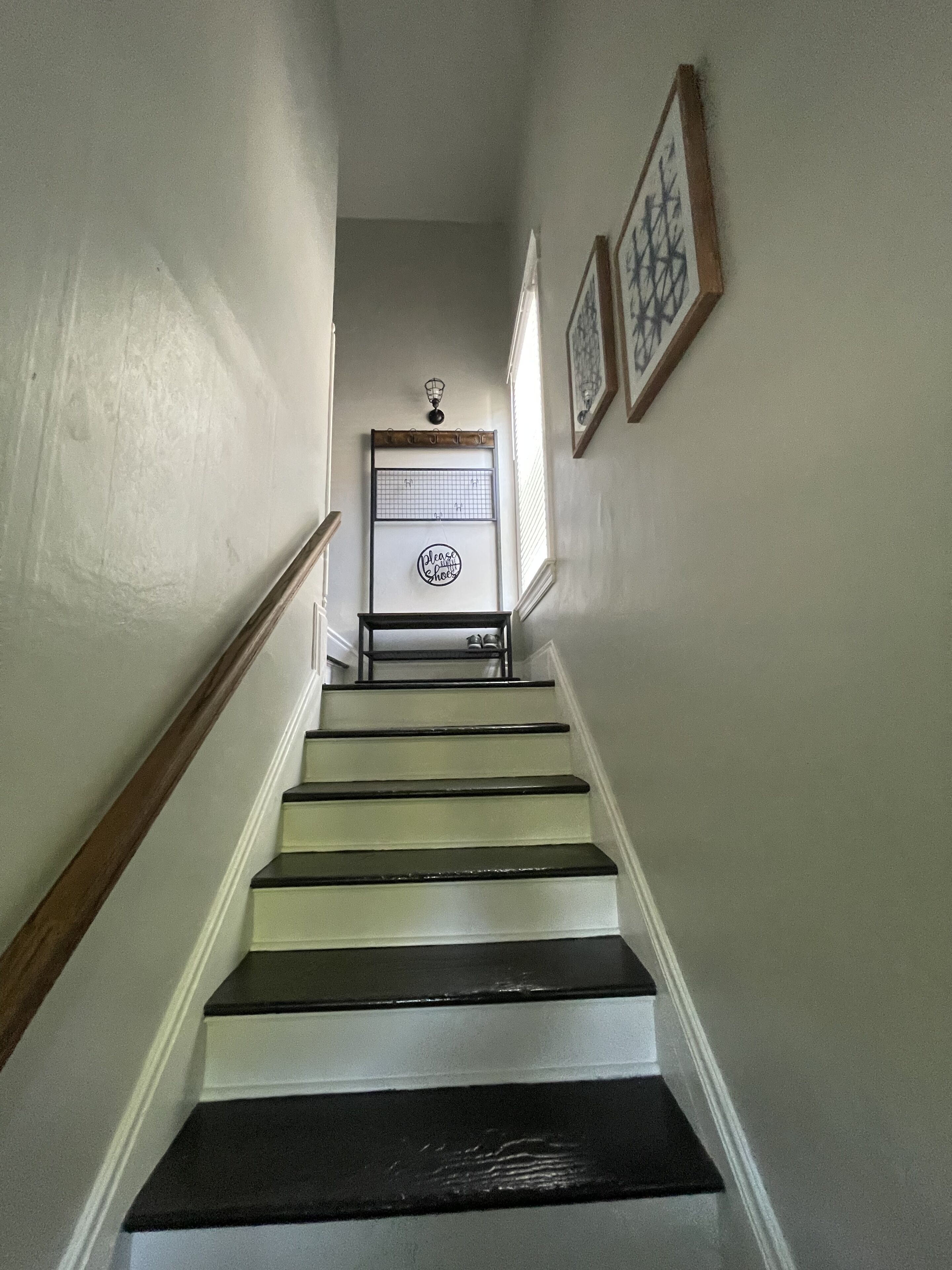 A staircase with alternating black and white steps, a wall-mounted light fixture, and two framed pictures.