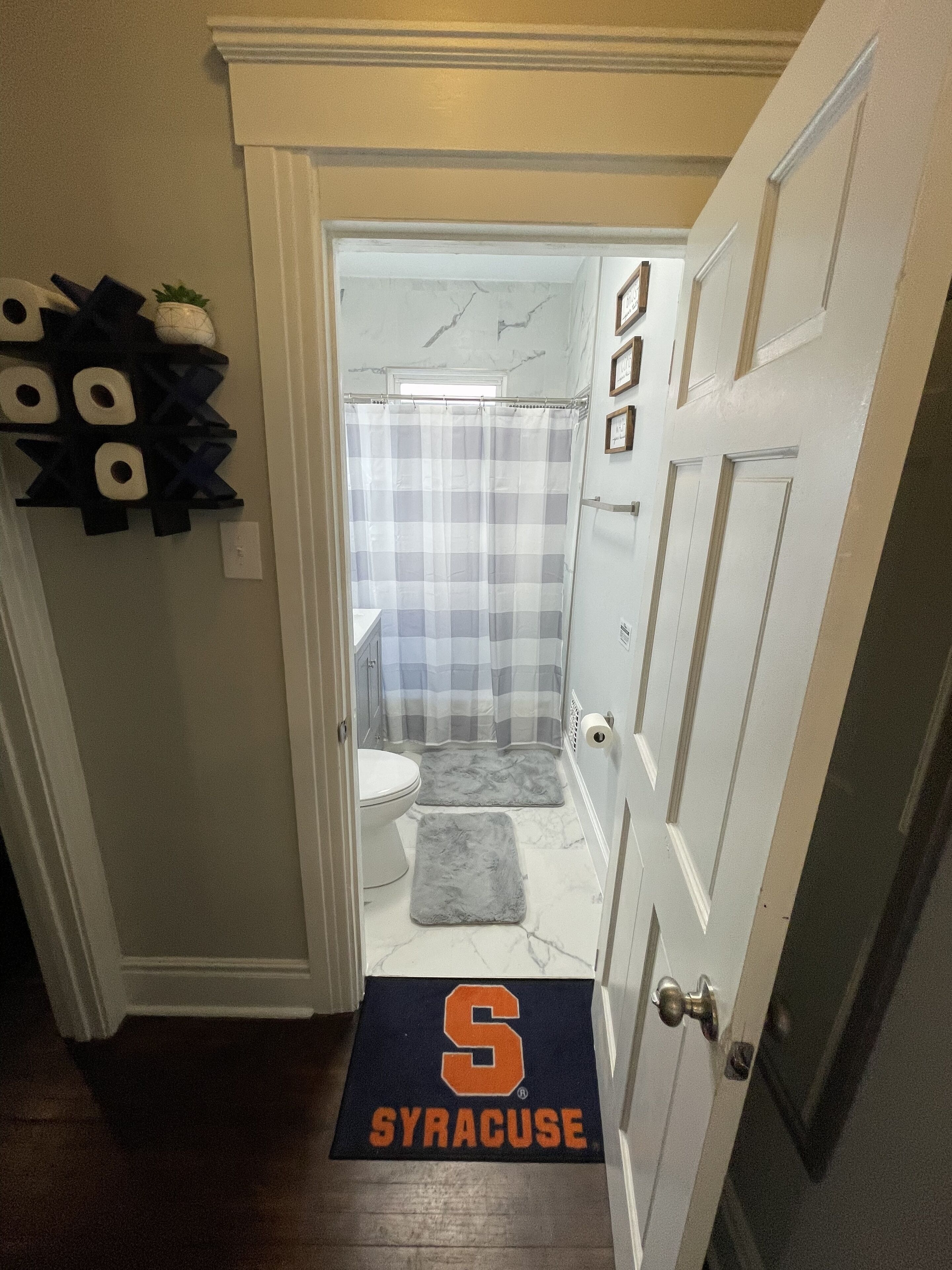 A bathroom with a shower, toilet, and a rug with 'Syracuse' on it.