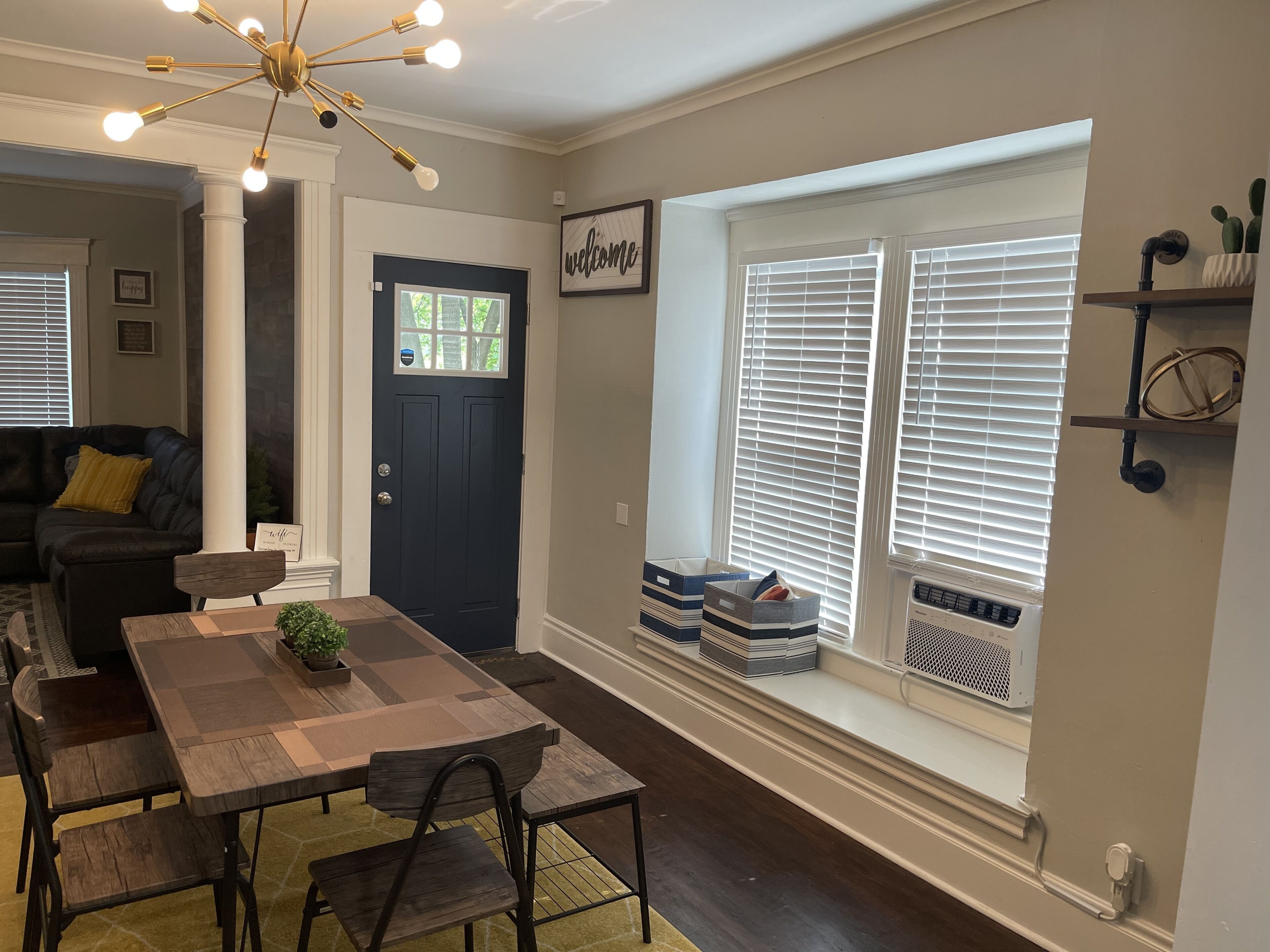 A dining area with a wooden table and chairs, a dark blue door, and a window with blinds.