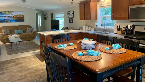 A modern kitchen with wooden cabinets, a central island, and a dining area with chairs and placemats.