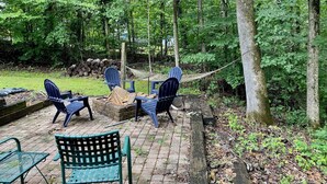 An outdoor seating area with chairs and a table, surrounded by trees and a hammock.