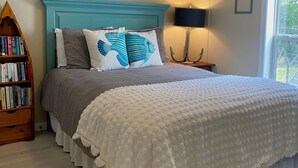 A bedroom with a teal headboard, a white quilted bedspread, and a bookshelf with books.
