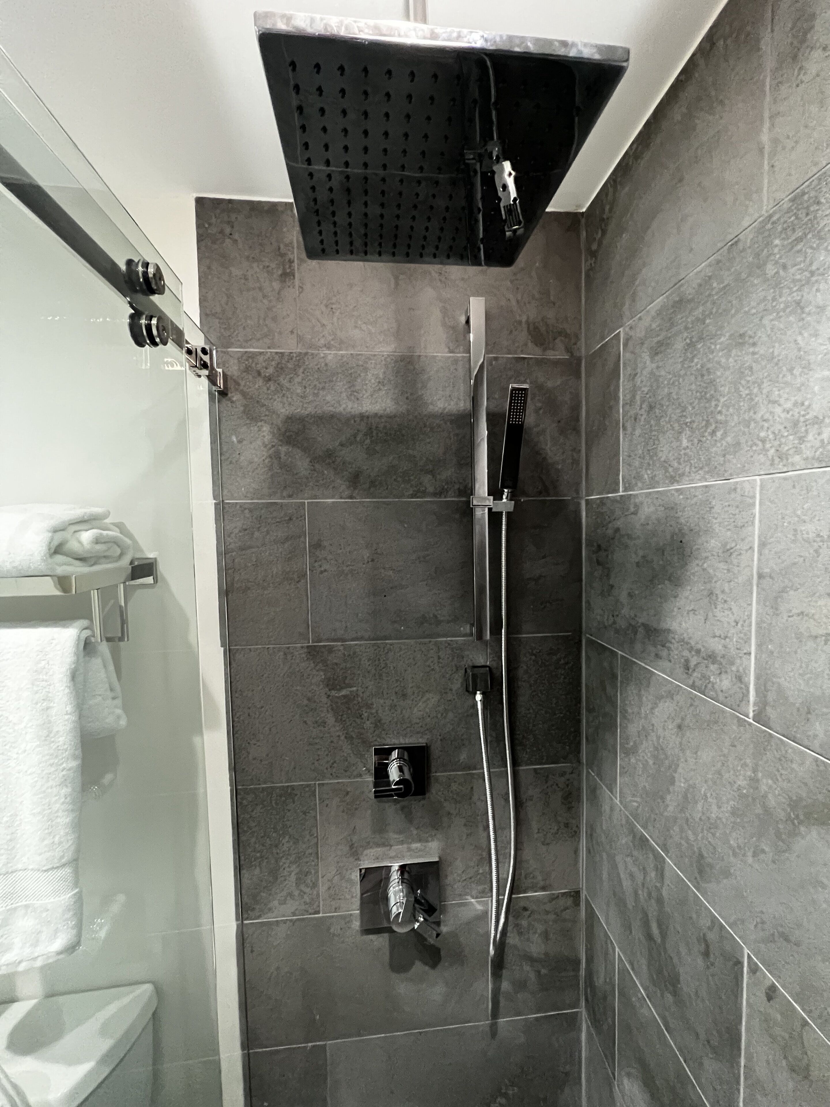 A shower with a handheld showerhead, a wall-mounted faucet, and a control panel.