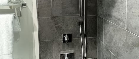 A shower with a handheld showerhead, a wall-mounted faucet, and a control panel.