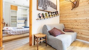 A cozy room with a bed, a small wooden stool, a grey sofa with patterned cushions, a wall-mounted wine rack, and a framed picture of a snowy forest. - The Loving Cabin  (Pragelato-Ruà)