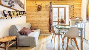 A cozy room with a wooden wall, a sofa, a dining table with chairs, and a wine rack with bottles. - The Loving Cabin  (Pragelato-Ruà)