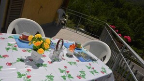 Ein Tisch draußen gedeckt, mit einer blumigen Tischdecke, einer Vase voller gelber Blumen und einem Teekessel.