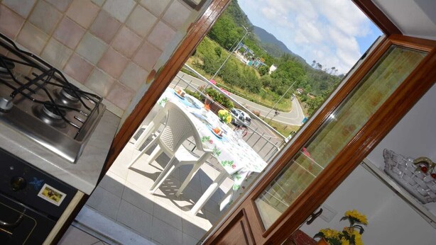 Eine Küche mit Gasherd, ein Essbereich mit Tisch und Stühlen sowie ein Blick auf eine Straße und Grünflächen.