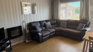 A living room with a leather sofa, a television, a vacuum cleaner, and a window with curtains.