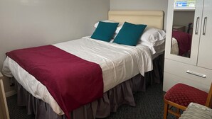 A single bed with white and teal bedding, a red throw blanket, and a mirror cabinet with a red cushion.