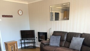 A living room with a brown leather sofa, a television, a small wooden table, and a mirror on the wall.