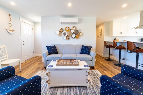 A living room with a sofa, two armchairs, a coffee table, and a wall-mounted decorative piece. - Newly remodeled cottage on a shell street in Siasconset, MA - Nantucket Island (Siasconset)