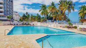 Una piscina con cubierta de piedra, rodeada de palmeras y una cerca blanca.