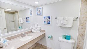 A bathroom with a sink, mirror, toilet, and two framed artworks on the wall. - Stunning Ocean Front Efficiency (Myrtle Beach)