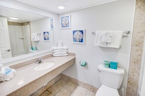 Un baño con lavamanos, espejo, inodoro y dos obras de arte enmarcadas en la pared.