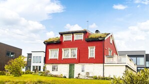 Une maison rouge à deux étages, avec une porte verte, des fenêtres blanches et un petit balcon doté d’une balustrade blanche.
