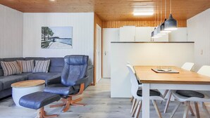 Ein modernes Wohnzimmer mit einer Couch, einem Esstisch mit Stühlen und einer Küchenzeile mit Schränken und Pendelleuchten.