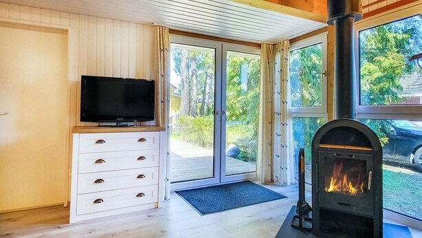 Ein modernes Wohnzimmer mit Kamin, einem Fernseher auf einer Holzkommode und großen Schiebegläsern, die auf eine Terrasse führen.