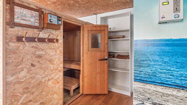 Interior em madeira com uma porta de madeira, uma prateleira com objetos e um quadro elétrico fixado na parede.