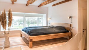 Quarto com cama de madeira, janela com vista para o exterior e um vaso com capim-do-campo.