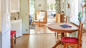 Una stanza accogliente con un tavolo da pranzo in legno, sedie imbottite rosse, un divano bianco e vista su un giardino attraverso una finestra.