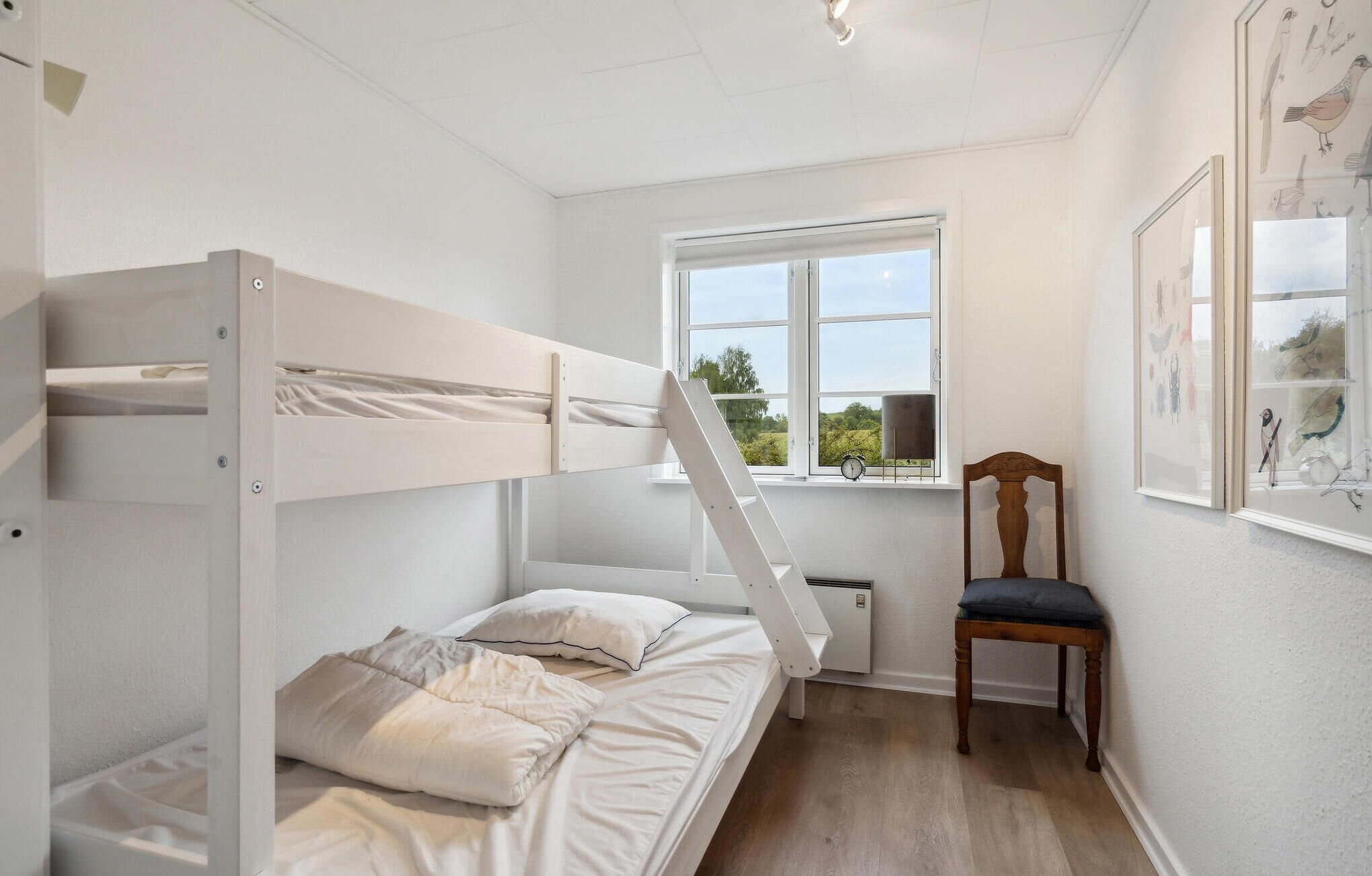 Een slaapkamer met een stapelbed, een raam, een stoel en kunst aan de muur.