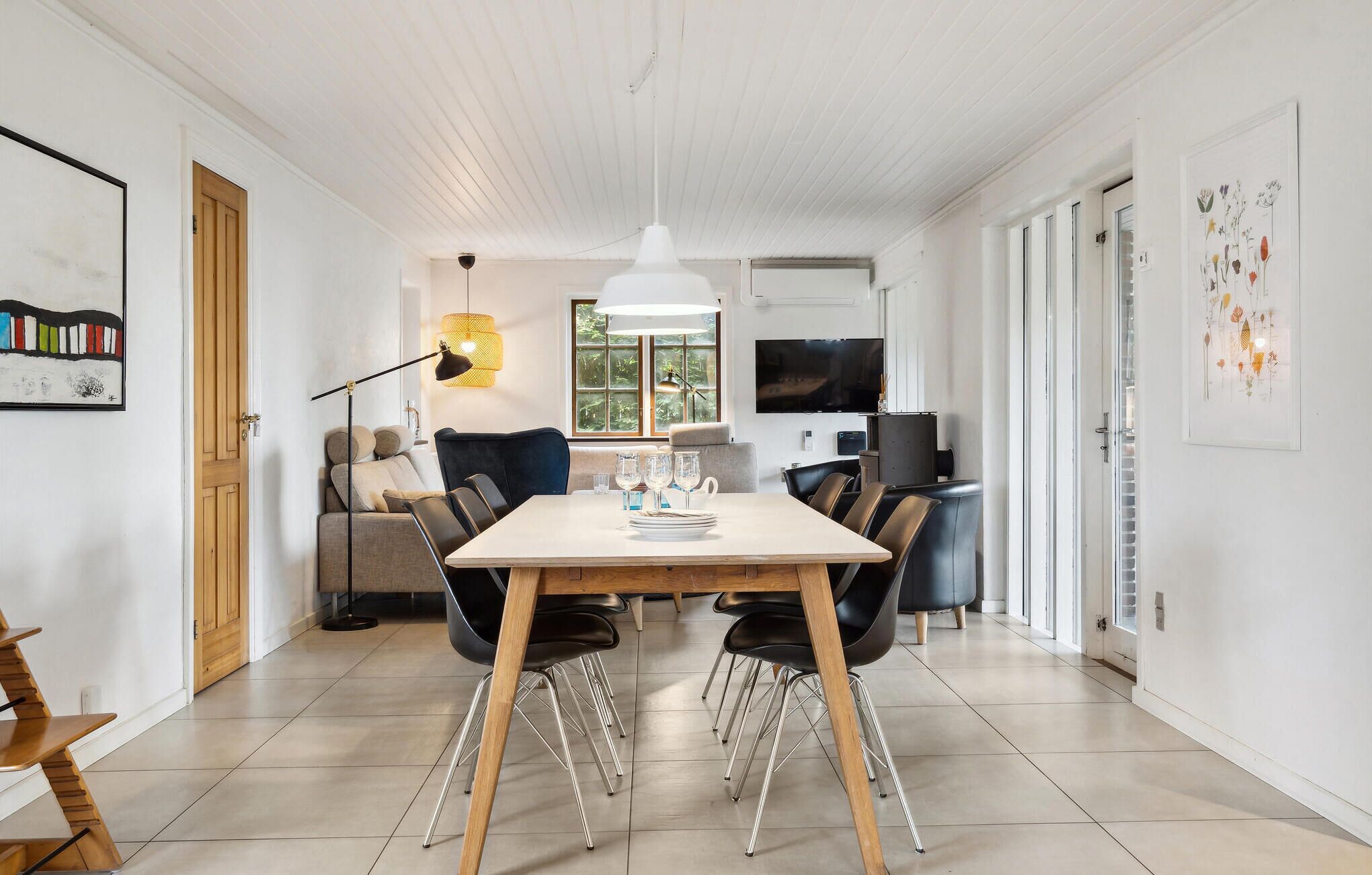 Een moderne eetruimte met een houten tafel, zwarte stoelen en een witte hanglamp.