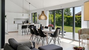 Une cuisine moderne avec des meubles blancs, un coin repas avec des chaises noires et de grandes portes-fenêtres coulissantes donnant sur un jardin.