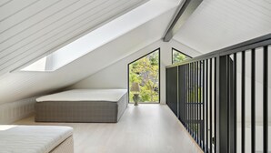 Une chambre moderne aménagée dans les combles, dotée de fenêtres de toit, d’un lit et offrant une vue sur les arbres.