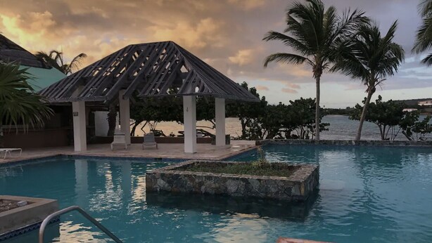 Área de piscina com um gazebo, palmeiras e céu ao pôr do sol.