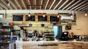 Uma cafeteria rústica com paredes de madeira, um balcão com equipamentos para preparar café e luminárias pendentes.