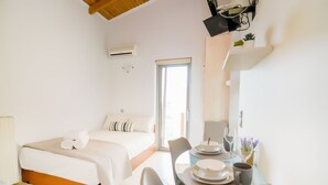 A hotel room with a bed, a dining table with plates and glasses, and a small plant on the wall. - Kallia Apartment (Chania)