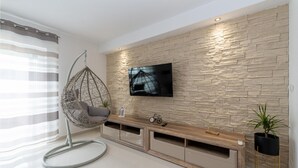 A modern living room with a hanging chair, a flat-screen TV mounted on a textured wall, a wooden console table, and a potted plant. - Amazing home in Benkovac (Benkovac)