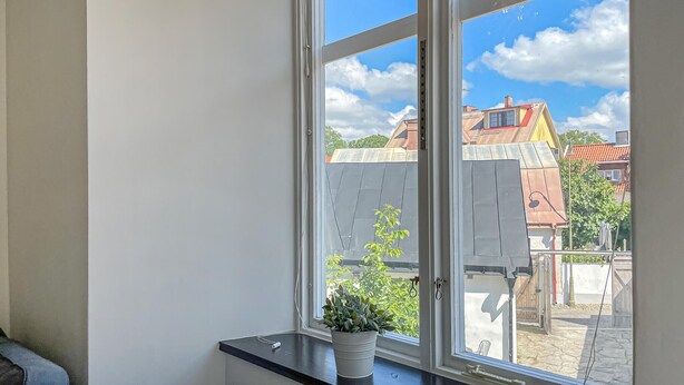 A room with a large window, a potted plant on the windowsill, and a view of neighboring buildings.