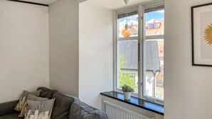 A room with a grey sofa, a radiator, a window with a view of buildings, and a framed picture on the wall.