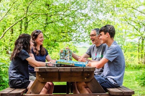 Four people seated around a wooden picnic table outdoors with greenery in the background. - Luxury Woodland Safari Tent with Private Hot Tub (Acton Scott)