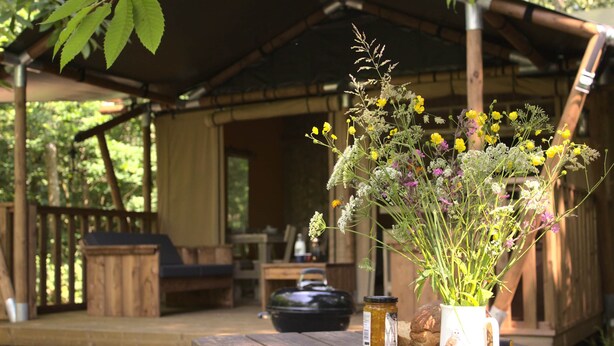 A rustic wooden table with a floral arrangement, jars, and a rustic pot in a covered outdoor area with wooden furniture and a wooden structure in the background. - Luxury Woodland Safari Tent with Private Hot Tub (Acton Scott)