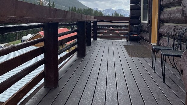 Een houten terras met banken en tafels, met uitzicht op een bergachtig landschap.