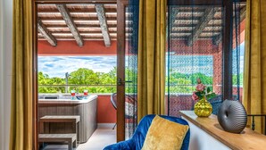 Un balcon avec un jacuzzi, une chaise bleue et une fenêtre donnant sur un paysage verdoyant.
