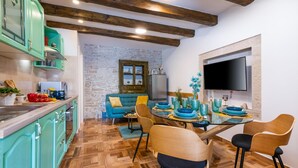 Une cuisine avec des armoires de couleur turquoise, un mur en pierre, une table à manger en bois avec des assiettes bleues et un téléviseur fixé au mur.
