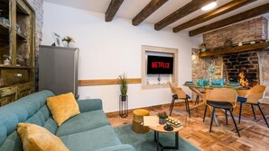Un salon chaleureux avec un canapé bleu, des poutres en bois, une cheminée en pierre et un téléviseur affichant le logo « NETFLIX ».