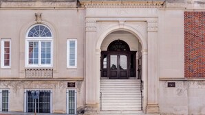 Un bâtiment à la façade classique, doté d’une grande entrée en arc de cercle et d’une enseigne sur laquelle on peut lire « HOMMES ».