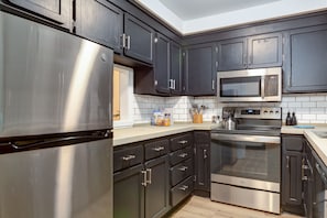 Una cocina moderna con electrodomésticos de acero inoxidable, armarios oscuros y salpicadero de azulejos.